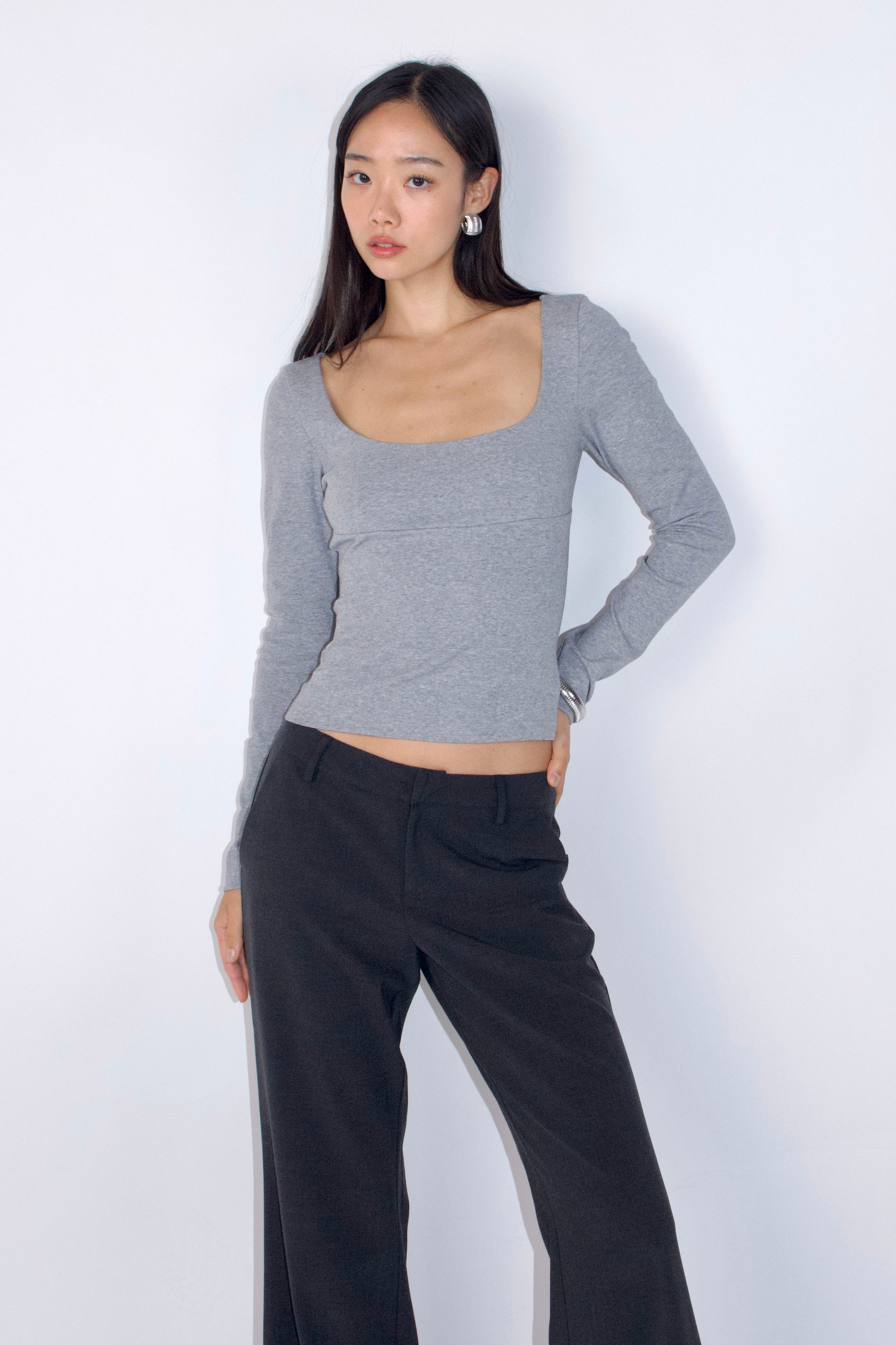 Woman wearing a gray long-sleeve top and black pants against a white background