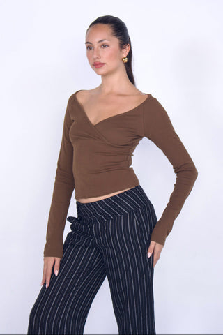 Woman wearing a brown long-sleeve top and black pinstripe pants on a white background