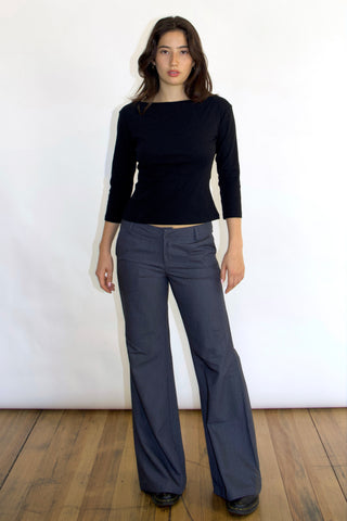 A woman wearing a 3/4 sleeve baby tee and wide-leg trousers. The top is black with a wide neckline and the trousers are gray with a visible texture.