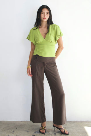 Woman wearing a green top and brown pants against a white background