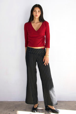 Woman wearing a red top and black pinstripe pants against a white background