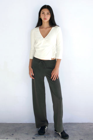 Woman wearing a white blouse and green pants against a white background