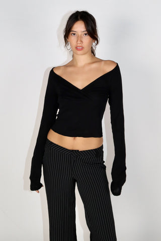 A model wearing a black V-neck long-sleeve top with a crop length and paired with striped pants.