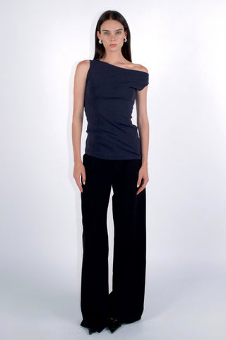 Woman wearing a navy one-shoulder top and black pants on a white background
