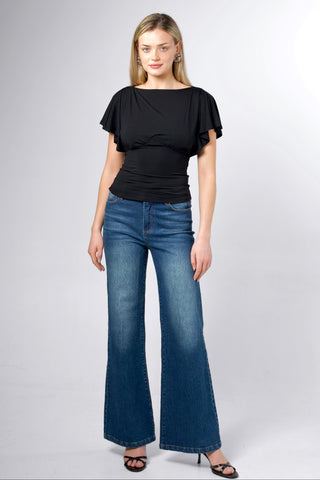 A woman modeling a black short-sleeve top with ruffled sleeves and blue wide-leg flare jeans against a light gray studio background.