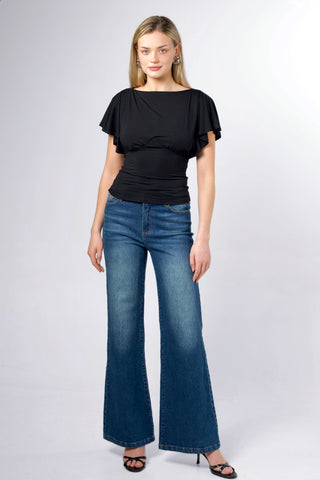 A woman modeling a black short-sleeve top with ruffled sleeves and blue wide-leg flare jeans against a light gray studio background.