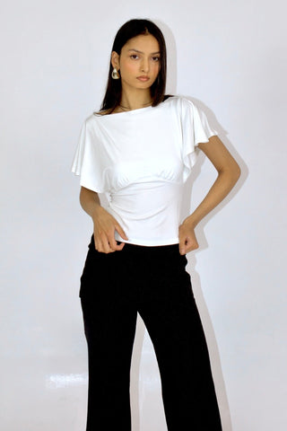 Woman wearing a white top and black pants against a plain background