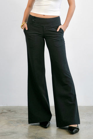 Person wearing black flared pants and a white top against a plain background