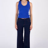 Woman wearing a blue tank top and dark jeans on a white background