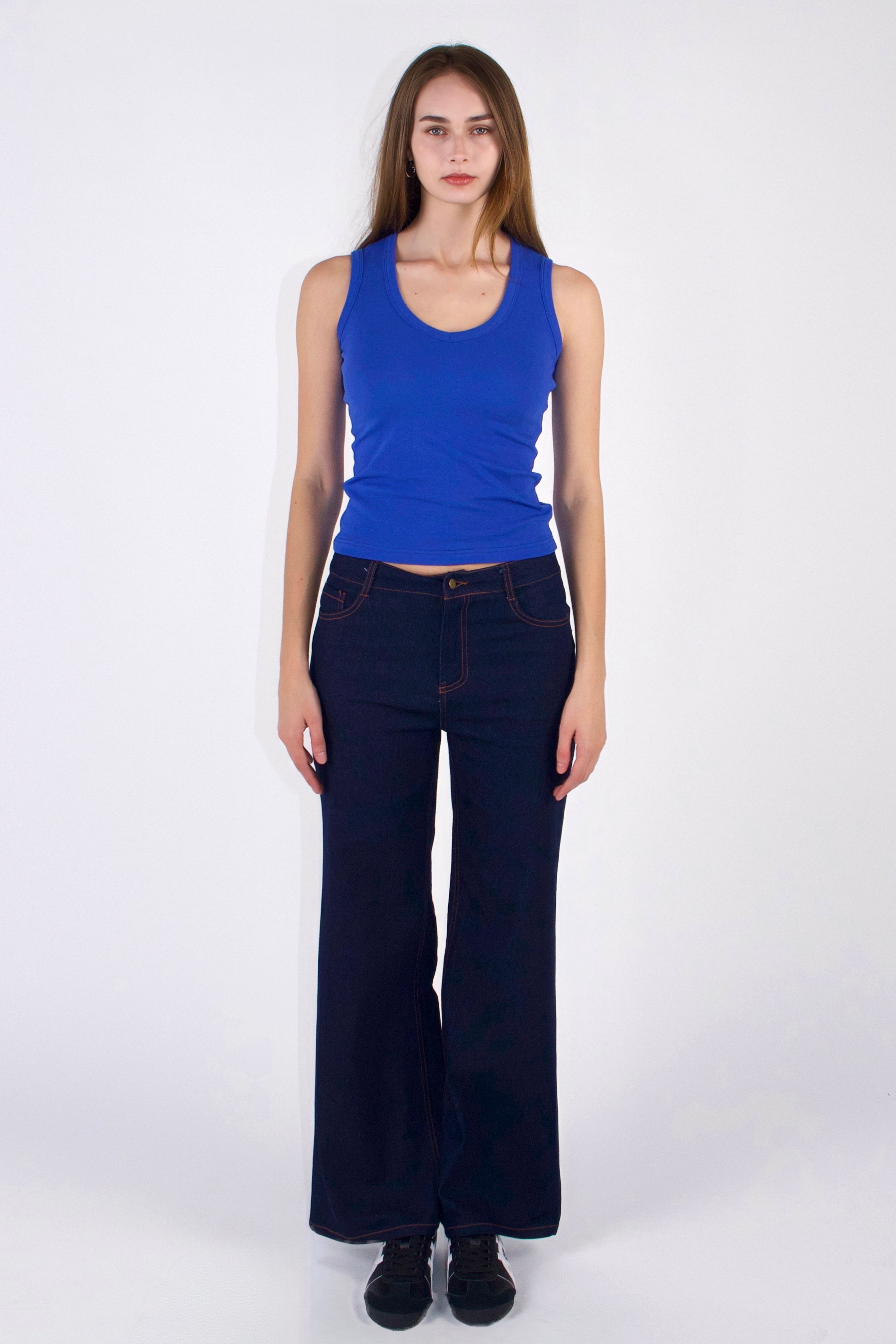 Woman wearing a blue tank top and dark jeans on a white background