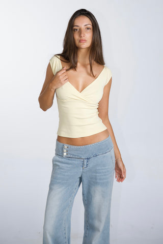 Woman wearing a light yellow top and blue jeans against a white background