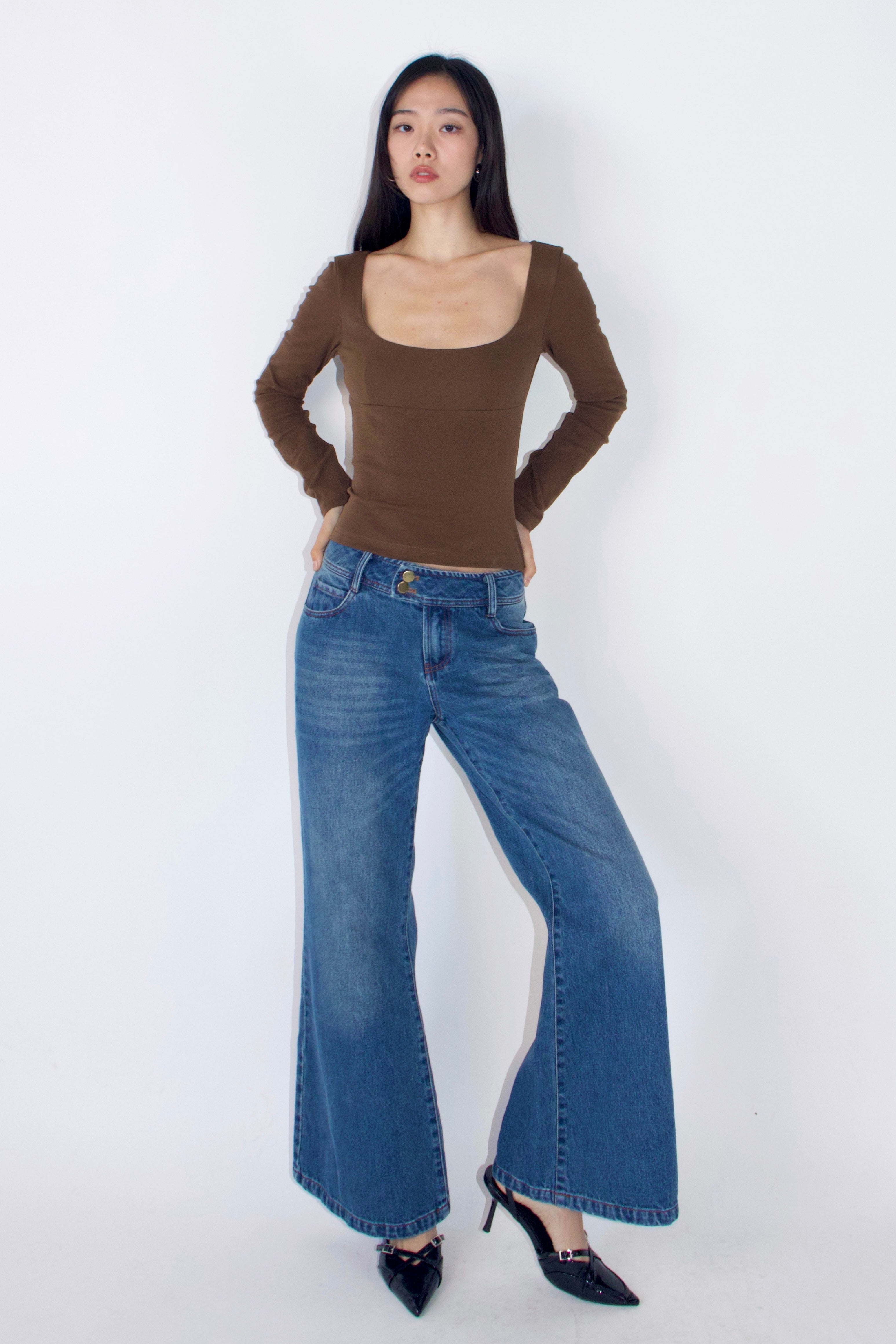 Woman wearing a brown top and blue jeans on a white background