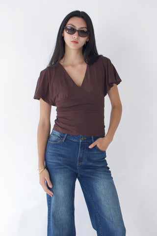Woman wearing a brown top and blue jeans against a white background