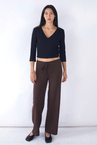 Woman wearing a black top and brown pants against a white background