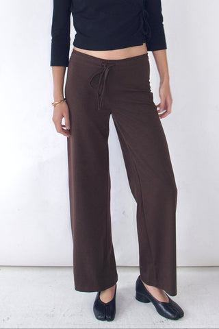 Woman wearing a black top and brown pants against a white background