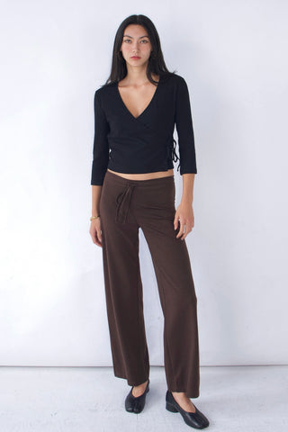Woman wearing a black top and brown pants against a white background