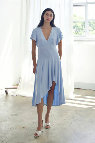 Woman wearing a light blue dress standing in a bright room with large windows.