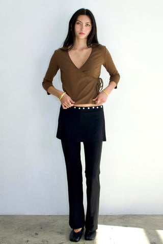 Woman wearing a brown top and black pants against a white background