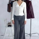 Woman wearing a white blouse and gray pants standing next to a rack with clothing and shoes.