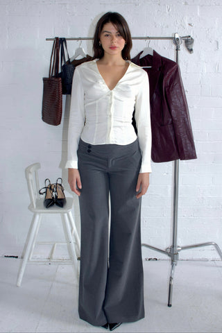 Woman wearing a white blouse and gray pants standing next to a rack with clothing and shoes.