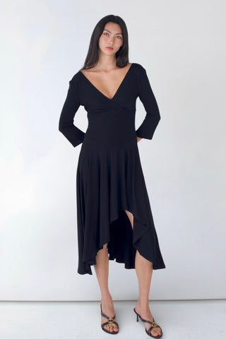 Woman wearing a black dress with long sleeves and an asymmetrical hem on a white background