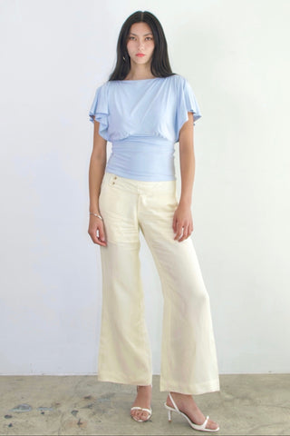 Woman wearing a light blue top and white pants against a plain background